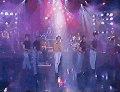 a group of people are standing on a stage in front of a stage with purple lights .