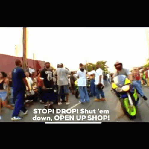 A Group Of People Are Standing On A Street With A Motorcycle In The Foreground And The Words Stop Drop Shut Em Down Open GIF