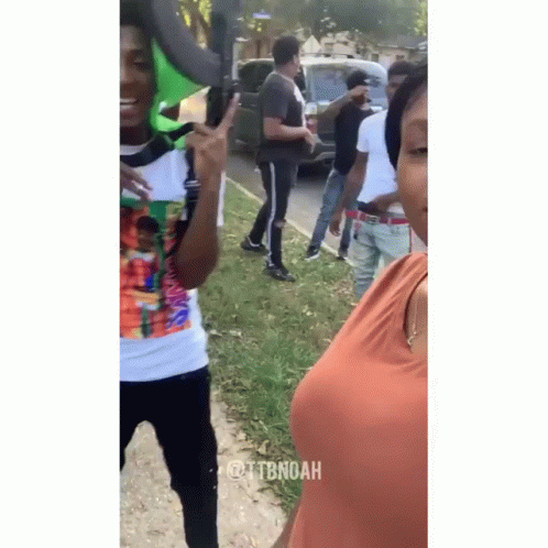 A Group Of People Are Standing On The Side Of The Road And One Of Them Is Giving The Peace Sign . GIF