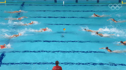 a group of people are swimming in a pool with the olympic rings on the wall