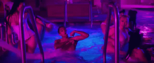 A Group Of People Are Swimming In A Swimming Pool At Night . GIF