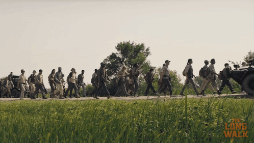 A Group Of People Are Walking Down A Road With The Words " The Long Walk " Written On The Bottom GIF