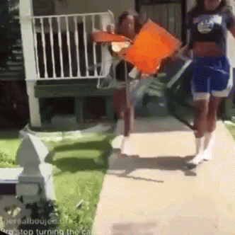 A Group Of People Are Walking Down A Sidewalk And One Of Them Is Holding An Orange Flag . GIF