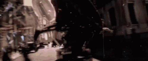 A Group Of People Are Walking Down A Street At Night In A Dark City . GIF