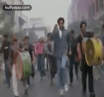 A Group Of People Are Walking Down A Street While Holding Drums . GIF