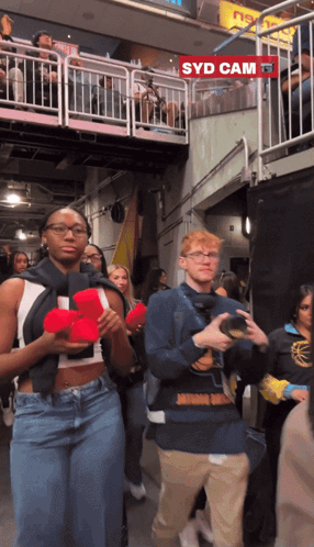 A Group Of People Are Walking In Front Of A Sign That Says Syd Cam GIF