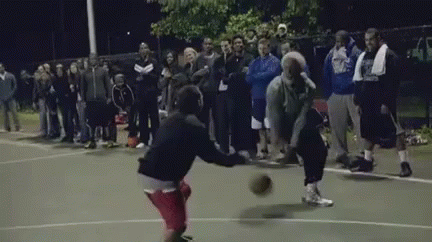a group of people are watching two men play basketball on a court at night