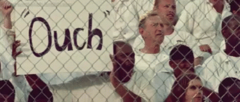 A Group Of People Behind A Chain Link Fence Holding A Sign That Says " Ouch " GIF