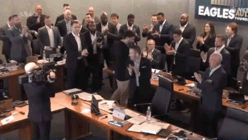 A Group Of People Clapping In Front Of A Sign That Says Eagles On It GIF