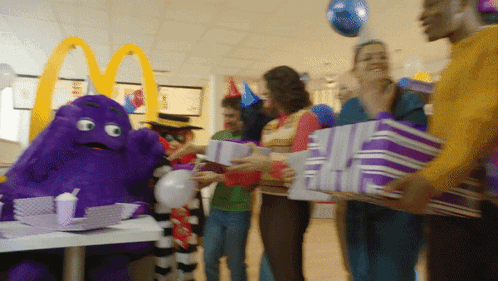 A Group Of People Holding Purple Gifts In Front Of A Mcdonald 'S Sign GIF
