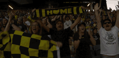 A Group Of People Holding Up A Scarf That Says " Home " GIF
