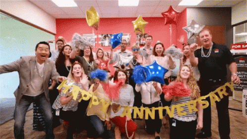 A Group Of People Holding Up Balloons And A Banner That Says Happy Anniversary GIF