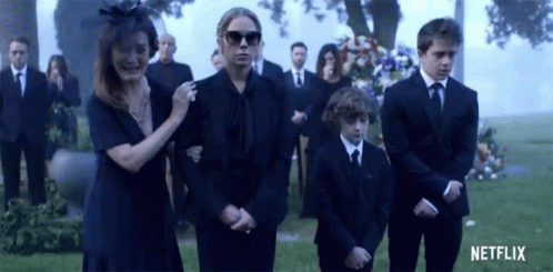 a group of people in black suits are standing in front of a grave .