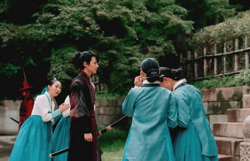 A Group Of People In Blue Dresses Are Standing Around A Man With A Sword GIF