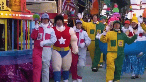 A Group Of People In Costumes Are Walking In A Parade With The Nbc Logo On The Bottom GIF