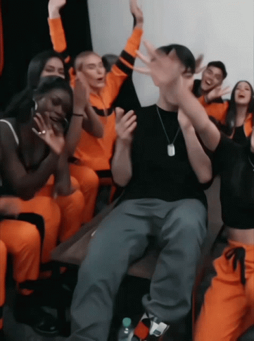 A Group Of People In Orange Jumpsuits Are Sitting Around A Table GIF