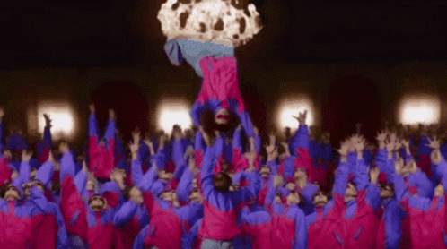 A Group Of People In Pink And Blue Jackets Are Standing In A Crowd And A Person Is Being Thrown In The Air . GIF