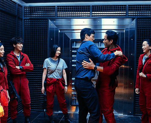 A Group Of People In Red Jumpsuits Are Hugging In Front Of A Vault Door GIF