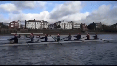 A Group Of People In Santa Hats Are Rowing On A River GIF