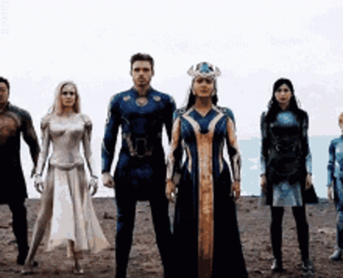 A Group Of People In Superhero Costumes Are Standing Next To Each Other In A Line . GIF