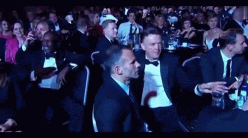 A Group Of People In Tuxedos Are Sitting In A Dark Room GIF