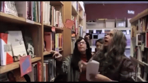 A Group Of People Looking At Books In A Library With A Sign That Says " Libros " GIF