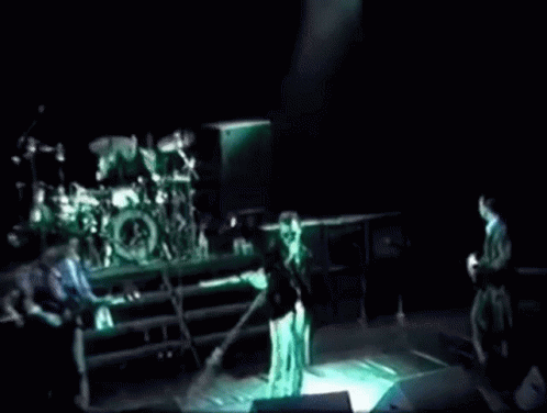 A Group Of People Playing Instruments On A Stage In A Dark Room . GIF