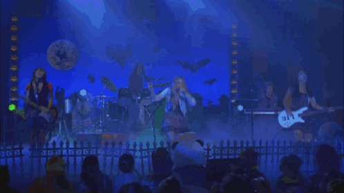 A Group Of People Playing Instruments On A Stage In Front Of A Sign That Says Gdg GIF