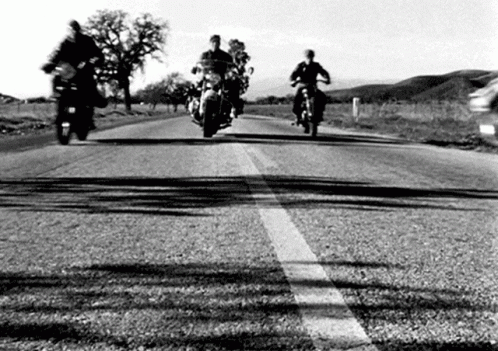A Group Of People Riding Motorcycles Down A Road . GIF