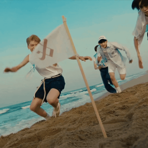 A Group Of People Running On A Beach With A Flag That Has The Letter P On It GIF