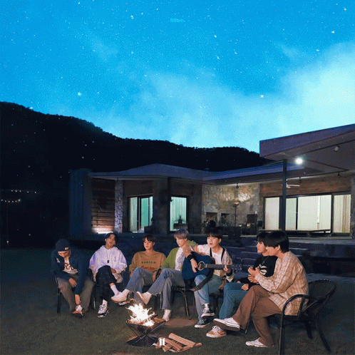 A Group Of People Sitting Around A Fire With One Wearing A Sweatshirt That Says ' Abercrombie ' On It GIF
