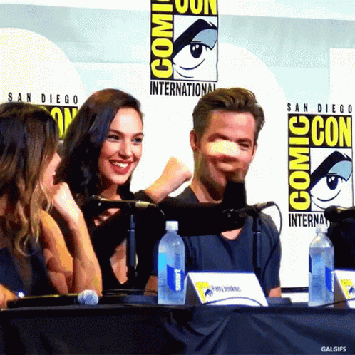 A Group Of People Sitting At A Table With A Comic Con Logo Behind Them GIF