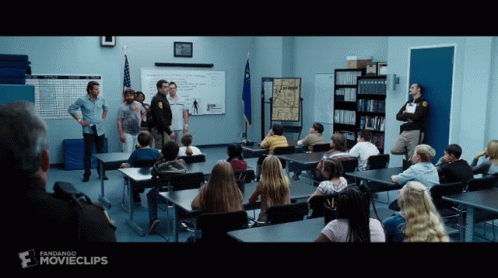A Group Of People Sitting At Desks In A Classroom With A Sign That Says Movieclips GIF