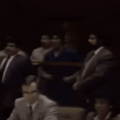 A Group Of People Sitting In A Dark Room With A Man Wearing A Badge That Says ' L.a. ' GIF