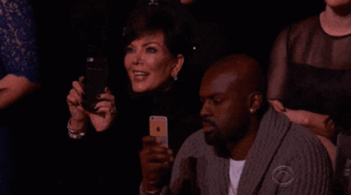 A Group Of People Sitting In A Dark Room With One Man Wearing A Sweater That Says Cbs On It GIF