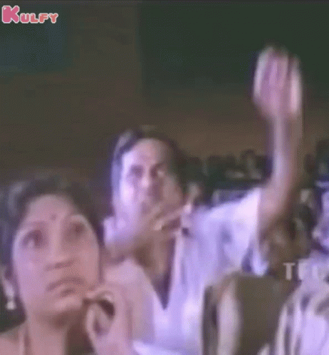 A Group Of People Sitting In A Dark Room With Their Hands In The Air GIF