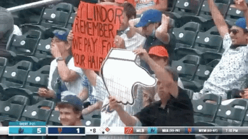 A Group Of People Sitting In A Stadium Holding Up Signs That Say Lindor Remember We Pay For Your Hair GIF