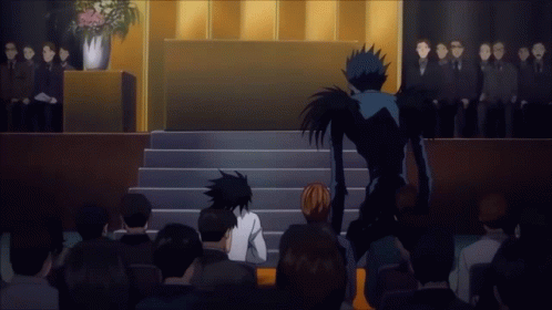 A Group Of People Sitting In Front Of A Podium With A Man In A Black Suit Standing Behind Them GIF