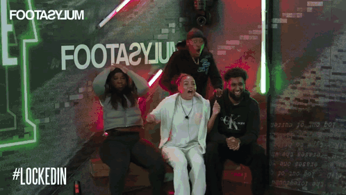 A Group Of People Sitting In Front Of A Sign That Says Foota2yjm GIF