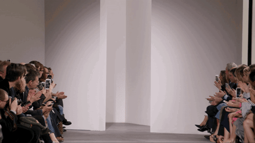 A Group Of People Sitting In Front Of A White Wall Looking At Their Phones GIF