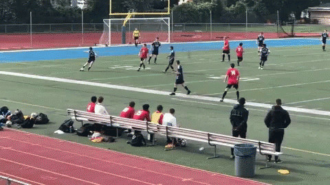 A Group Of People Sitting On A Bench Watching A Soccer Game With A Player Wearing A Red Jersey With The Number 19 On It GIF