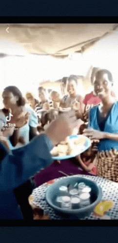 A Group Of People Standing Around A Table Eating Food . GIF