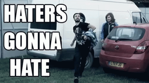 A Group Of People Standing In Front Of A Red Car And A White Van With The Words Haters Gonna Hate Written On It GIF