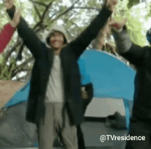 A Group Of People Standing In Front Of A Tent With Their Hands In The Air . GIF