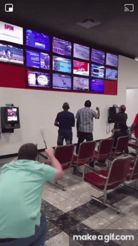 A Group Of People Standing In Front Of A Wall With A Screen That Says Spin GIF