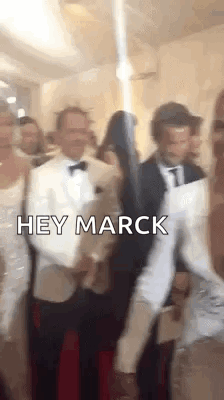 A Group Of People Standing Next To Each Other In A Room With The Words `` Hey Marck '' Written On The Screen . GIF
