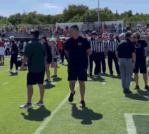 a group of people standing on a football field with one man wearing a shirt that says ' uc ' on it