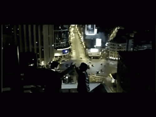 A Group Of People Standing On Top Of A Building Overlooking A City At Night GIF
