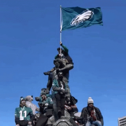 A Group Of People Standing On Top Of A Statue Holding A Flag With The Eagles Logo On It GIF