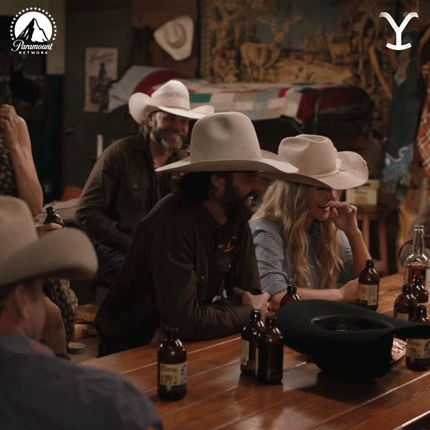 A Group Of People Wearing Cowboy Hats Sit At A Table With Bottles Of Beer And A Paramount Logo In The Background GIF